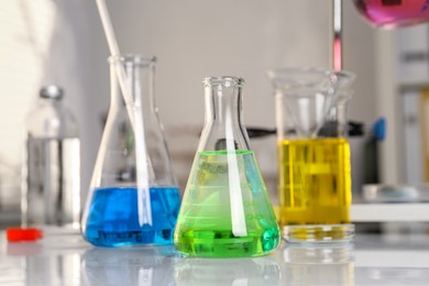 Photo of Laboratory analysis. Glassware with different liquids on white table indoors, closeup