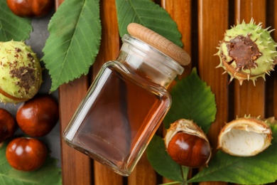 Photo of Chestnuts, leaves and jar of essential oil on wooden table, flat lay