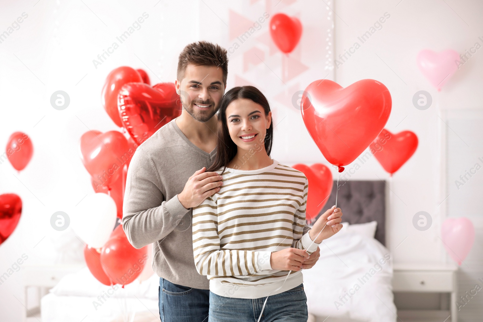 Photo of Lovely young couple in bedroom decorated with heart shaped balloons. Valentine's day celebration