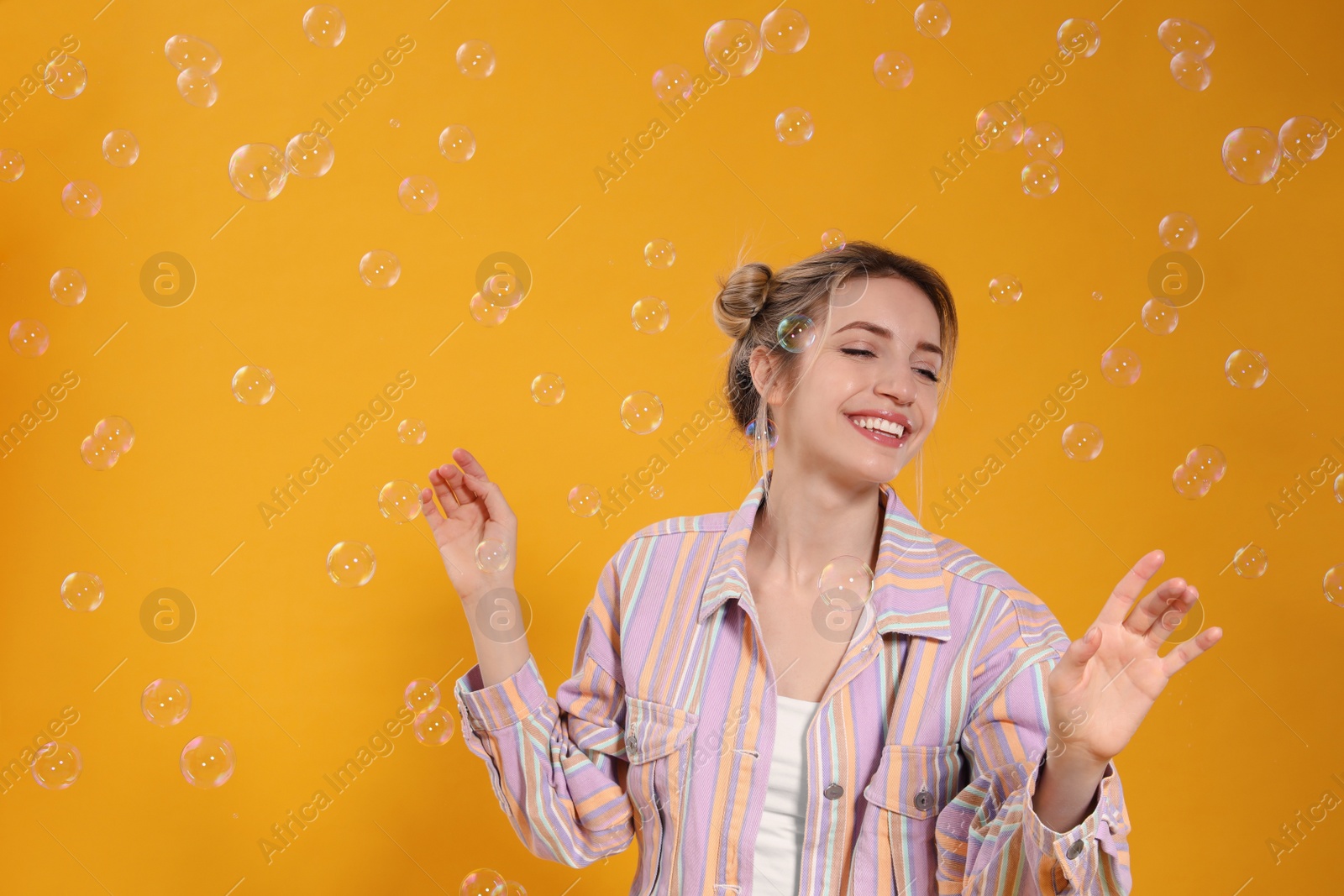 Photo of Young woman playing with soap bubbles on yellow background, space for text