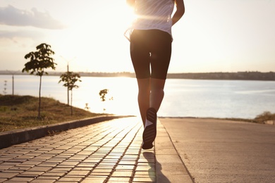 Photo of Young woman running near river in morning, closeup