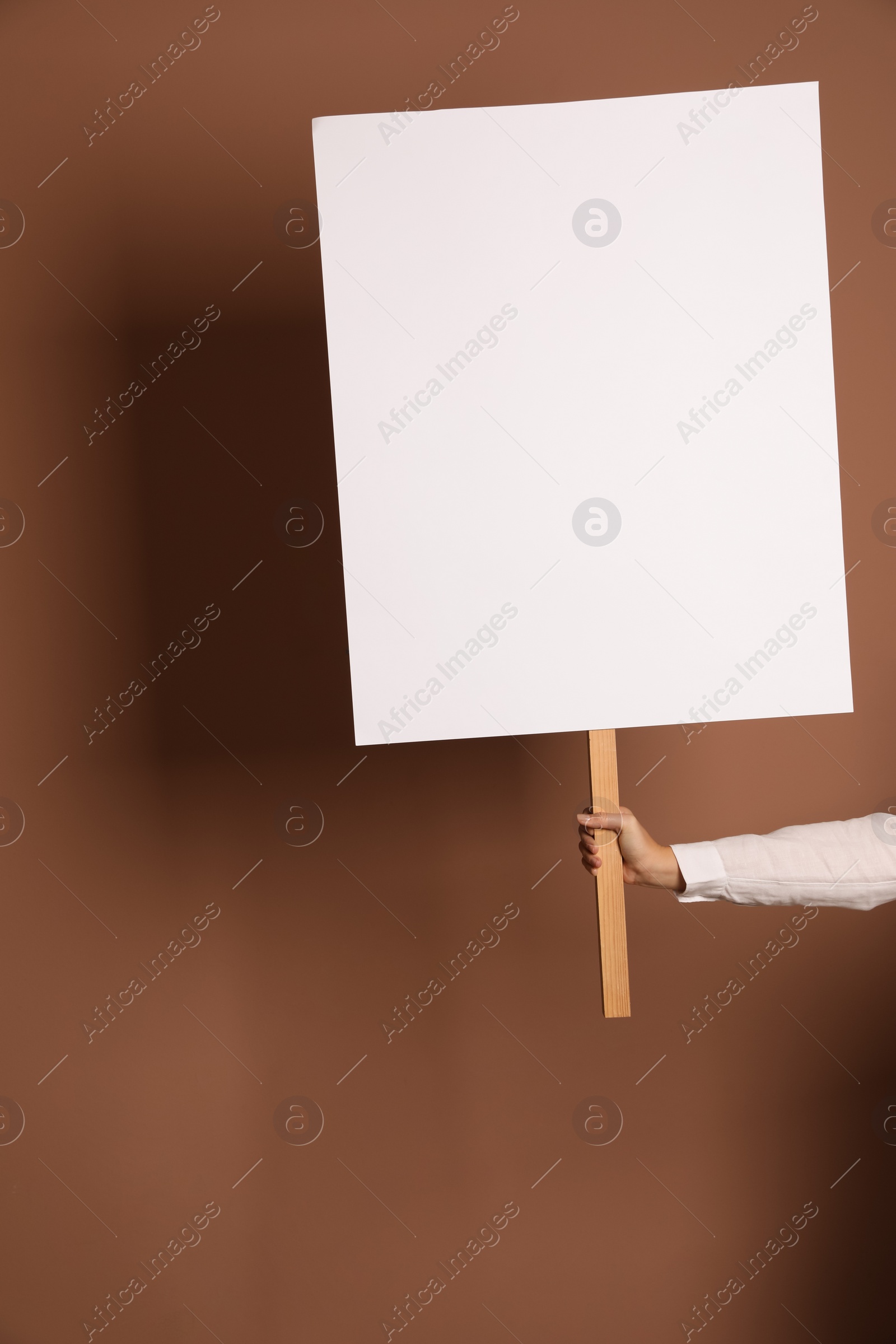 Photo of Woman holding blank sign on brown background, closeup. Space for design