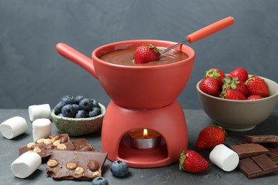 Photo of Fondue pot with melted chocolate, marshmallows, fork and different fresh berries on grey table