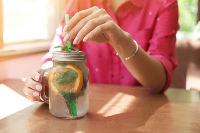 Young woman with mason jar of tasty natural lemonade in cafe, closeup. Detox drink