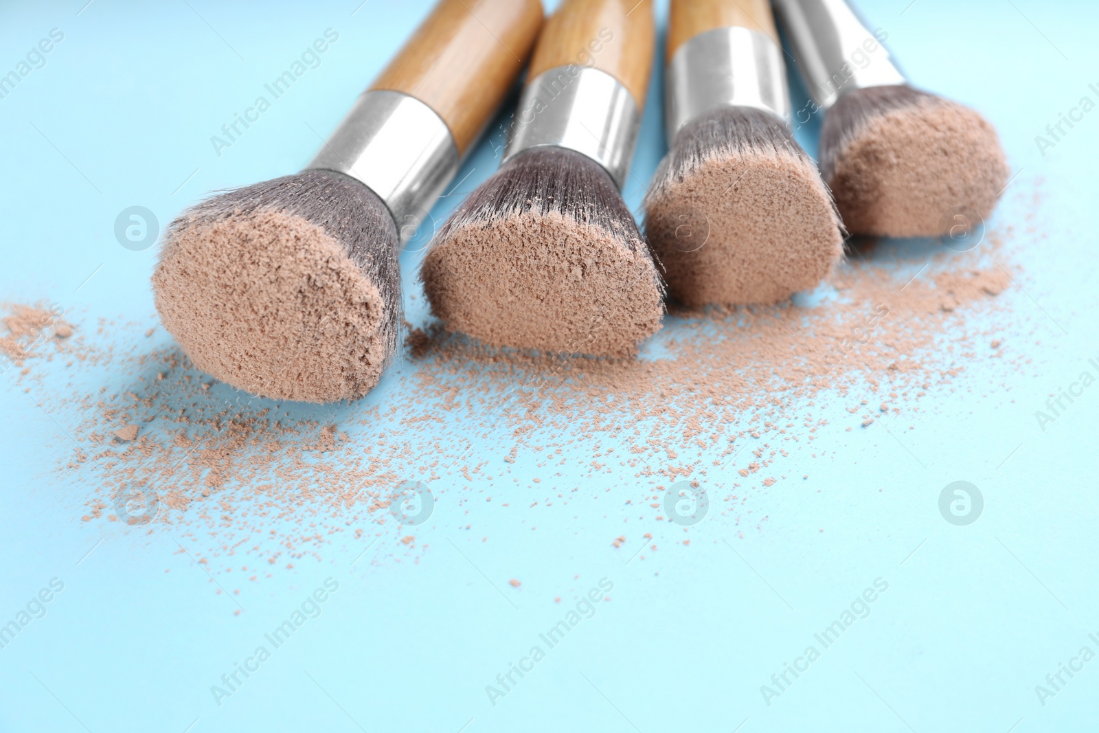 Photo of Different makeup brushes with crushed cosmetic product on light blue background, closeup