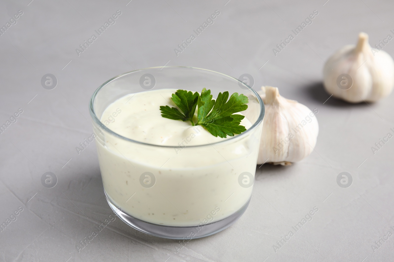 Photo of Fresh garlic bulbs and bowl of sauce on grey background