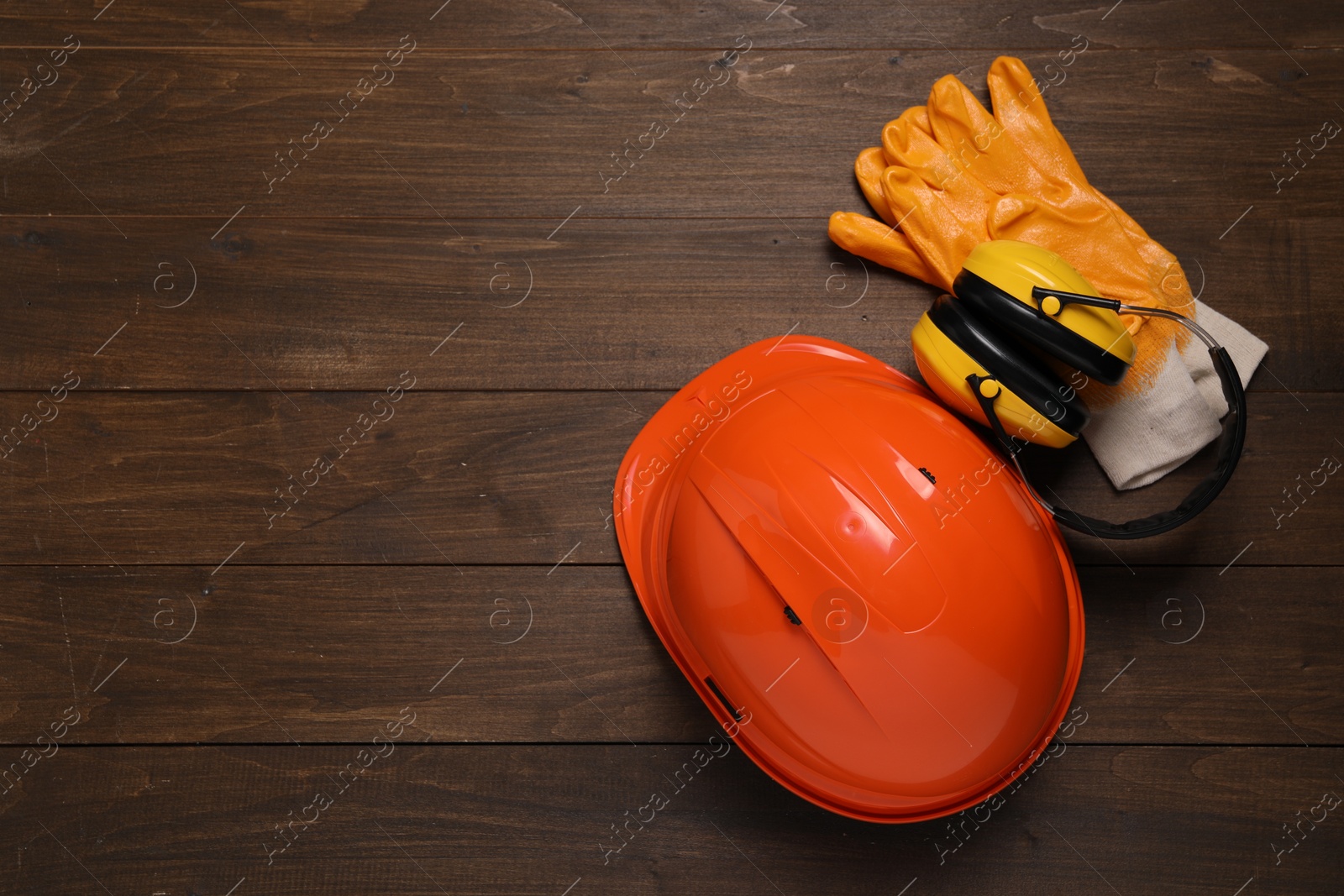 Photo of Hard hat, earmuffs and gloves on wooden table, flat lay with space for text. Safety equipment