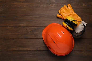 Hard hat, earmuffs and gloves on wooden table, flat lay with space for text. Safety equipment