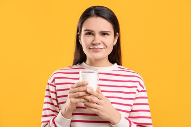 Cute woman with milk mustache holding glass of tasty dairy drink on yellow background