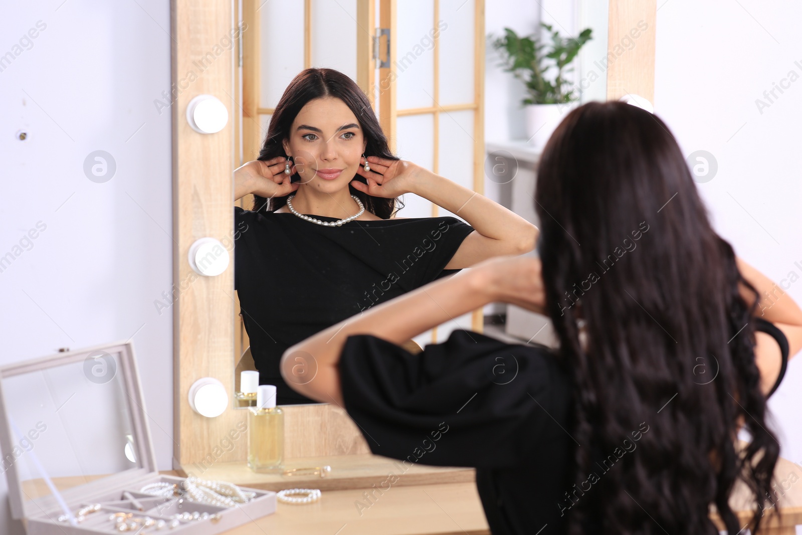 Photo of Young woman wearing elegant pearl jewelry near mirror indoors