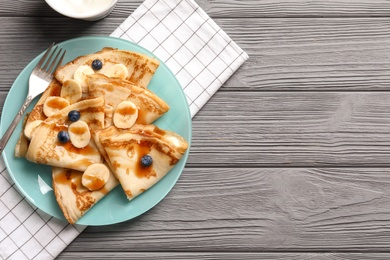 Photo of Thin pancakes served with syrup, berries and banana on plate, top view