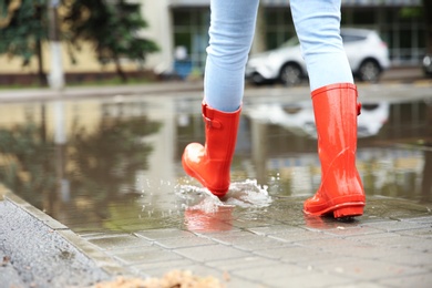 Photo of Woman with red rubber boots in puddle, closeup. Rainy weather