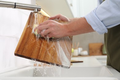 Photo of Man washing wooden cutting board in kitchen, closeup