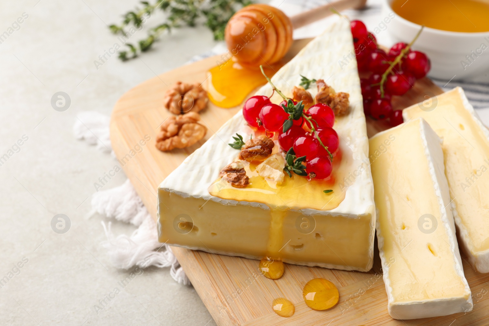 Photo of Brie cheese served with red currants, walnuts and honey on light table, closeup