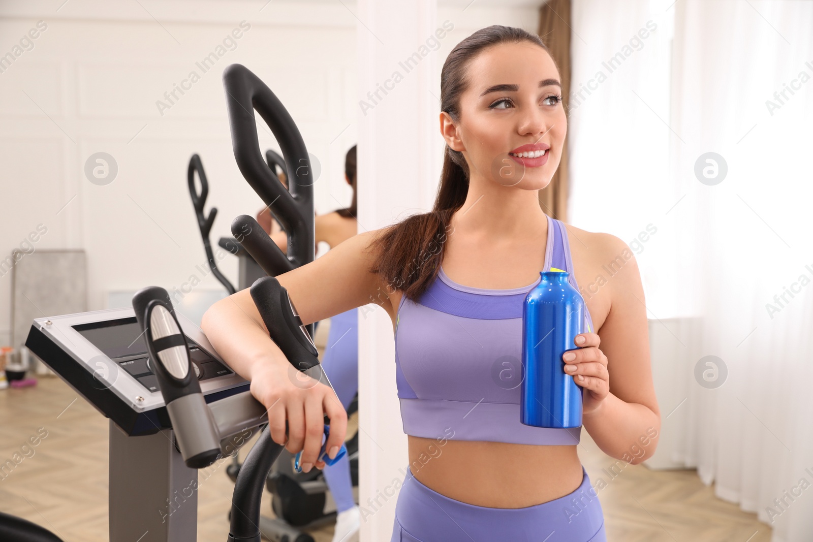 Photo of Woman with bottle near elliptical machine indoors