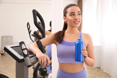 Photo of Woman with bottle near elliptical machine indoors