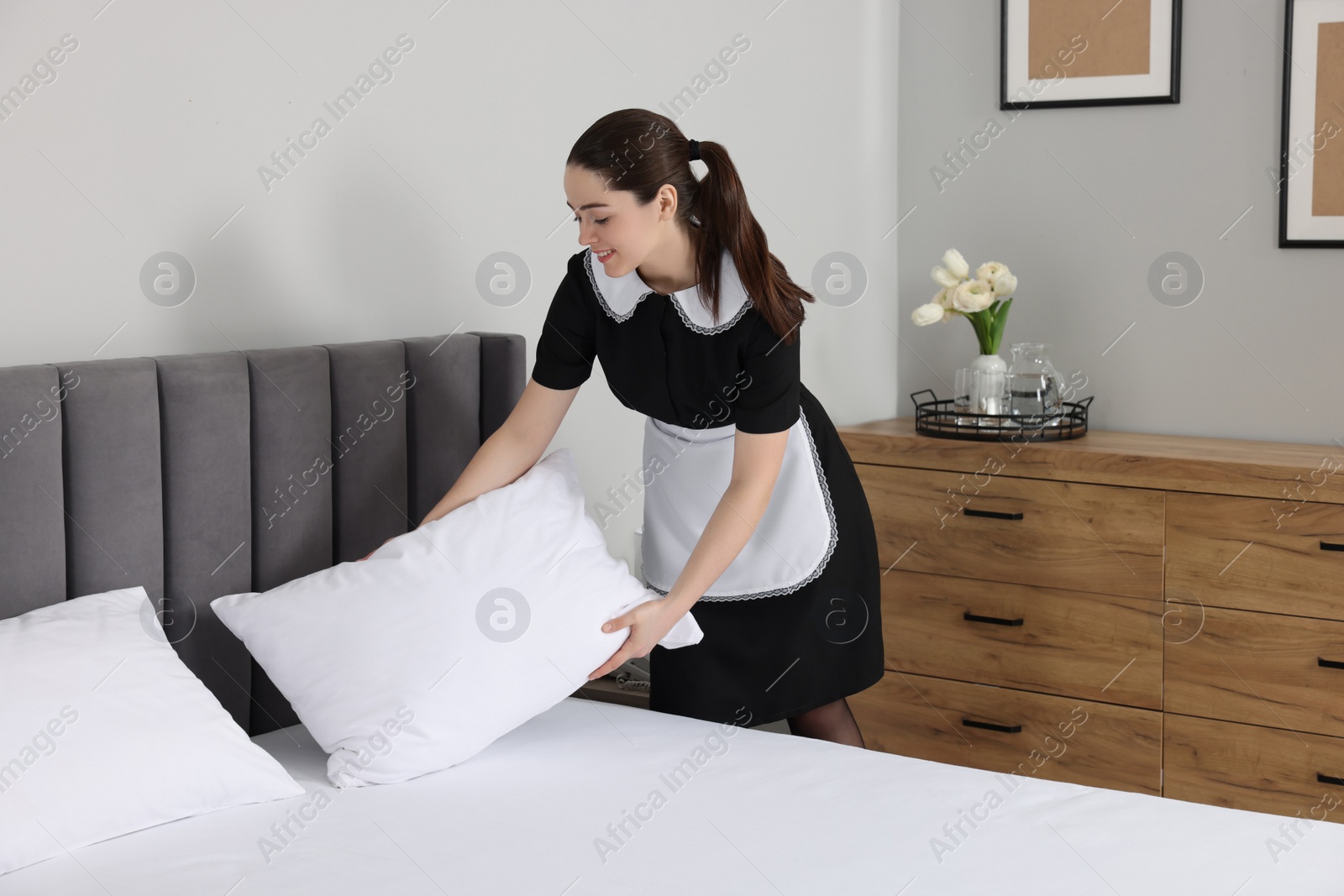 Photo of Young chambermaid making bed in hotel room