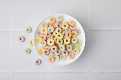 Photo of Cereal rings and milk in bowl on white tiled table, top view