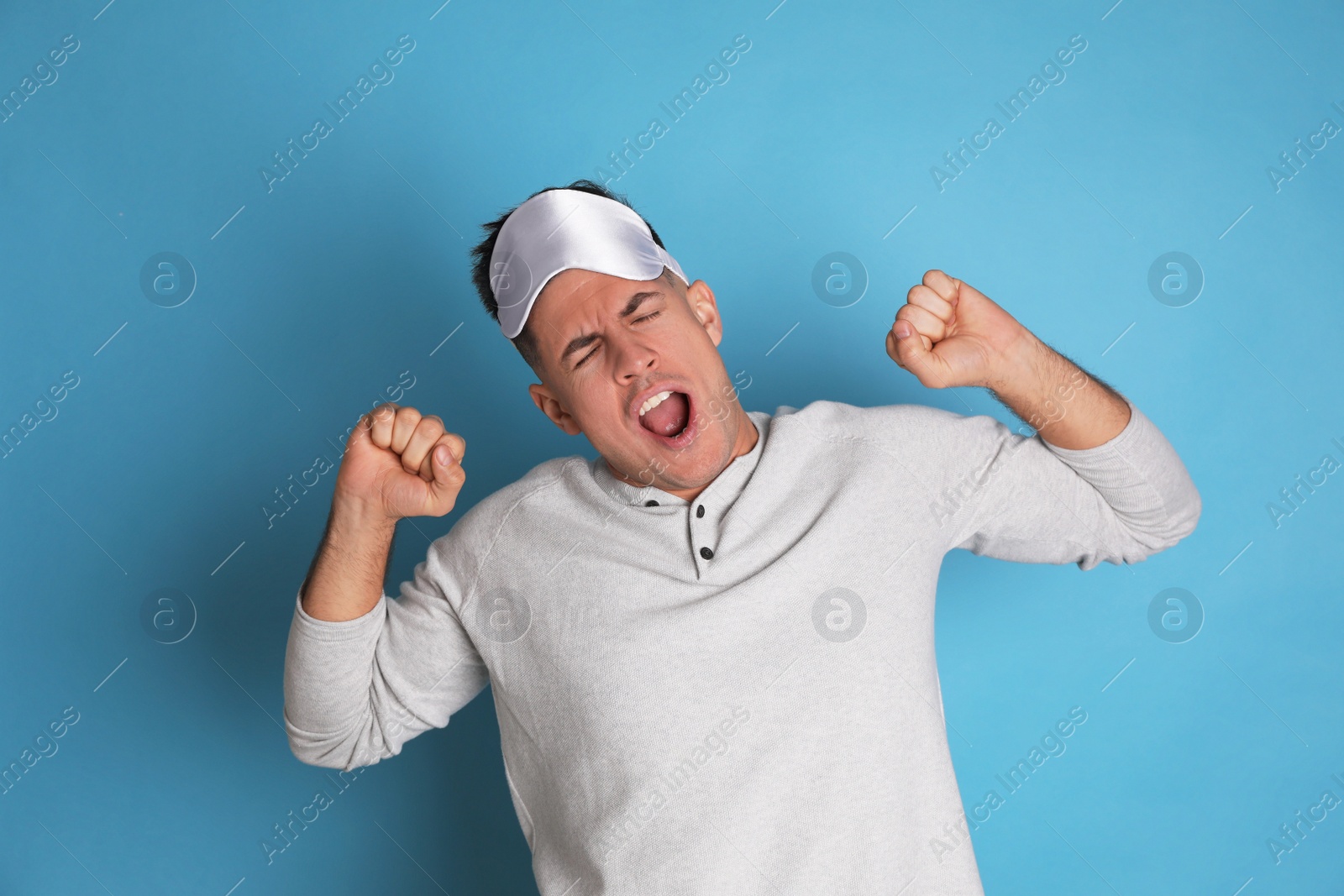 Photo of Tired man with sleeping mask yawning on light blue background