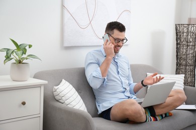 Photo of Businessman in shirt and underwear talking on phone during video call at home