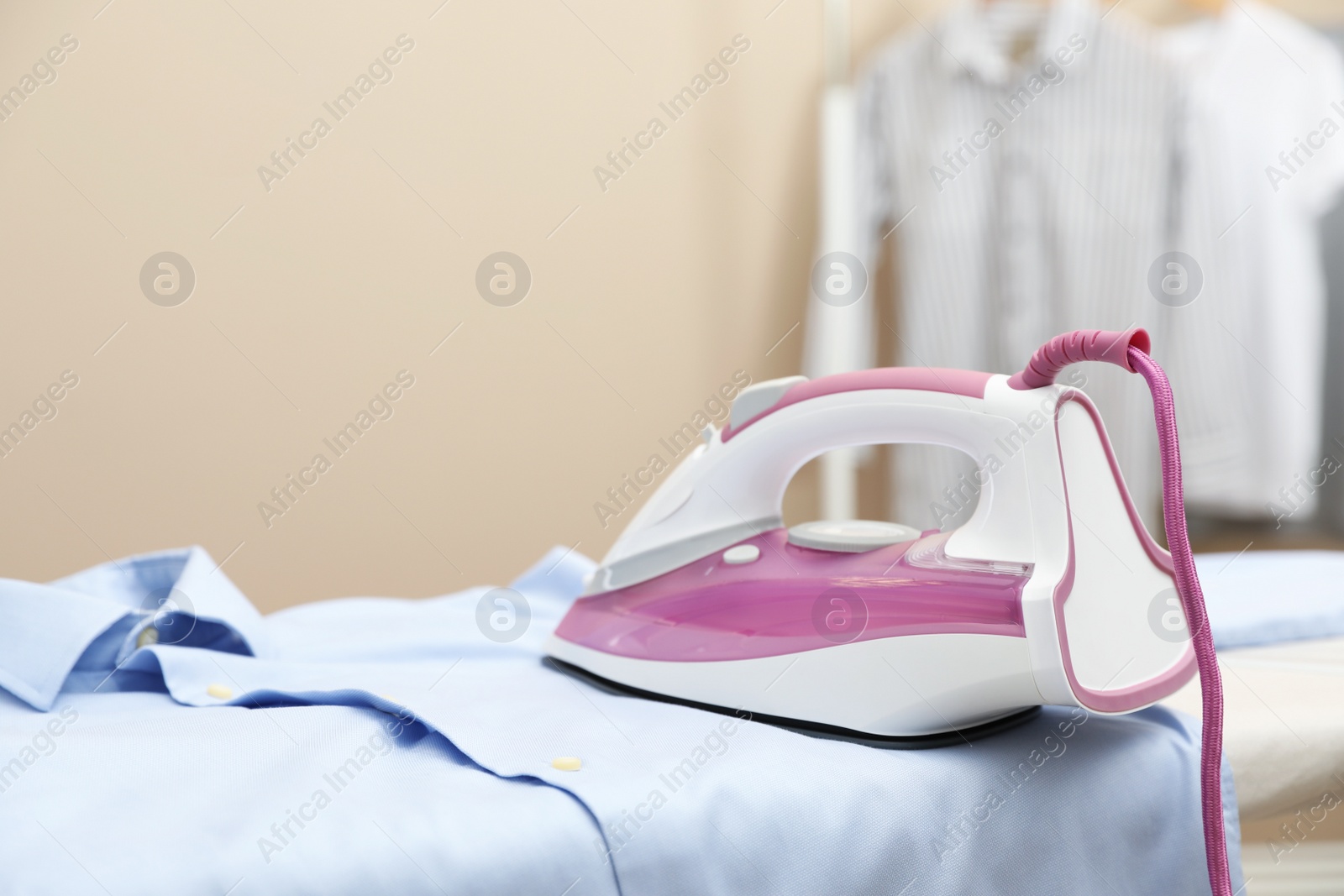 Photo of New modern iron and clean shirt on board against beige background, space for text. Laundry day