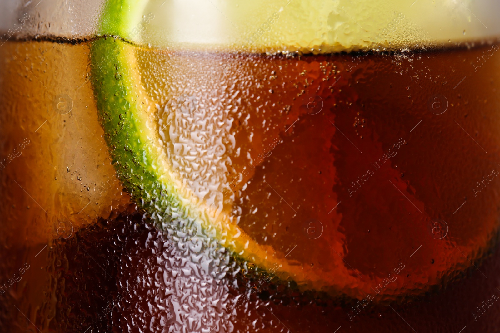 Photo of Glass of refreshing drink with sliced lime and ice cubes as background, closeup