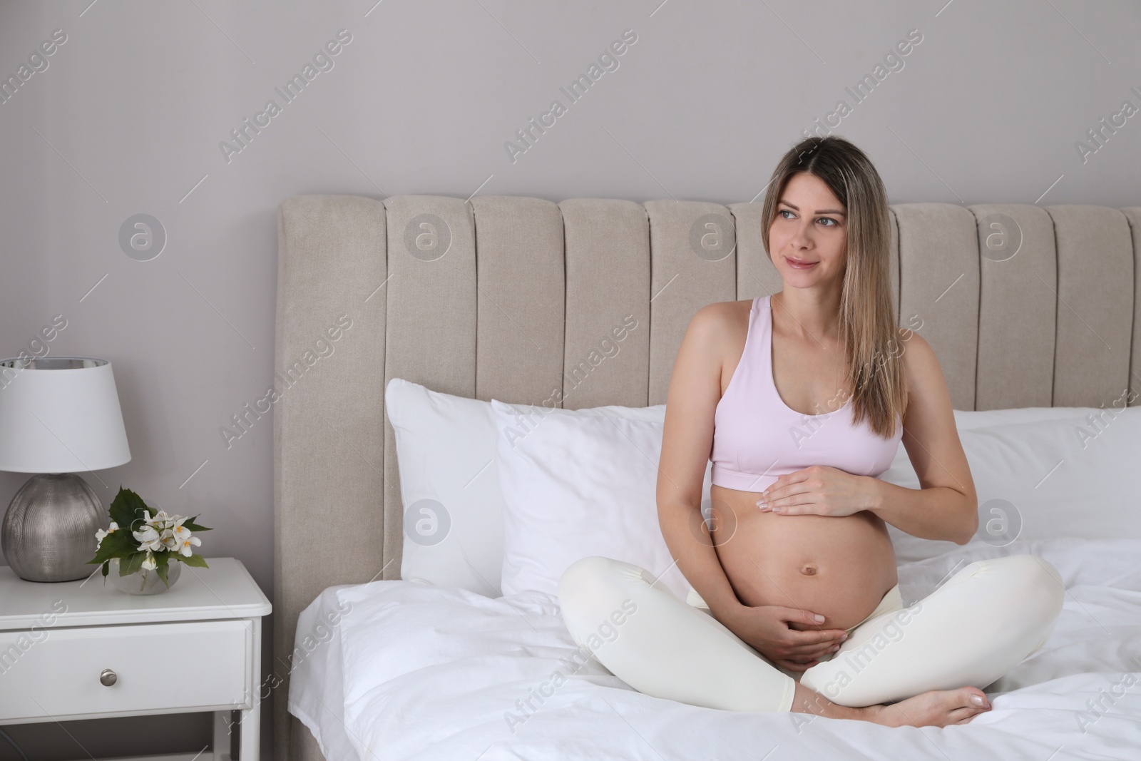 Photo of Beautiful pregnant woman sitting on bed at home. Space for text