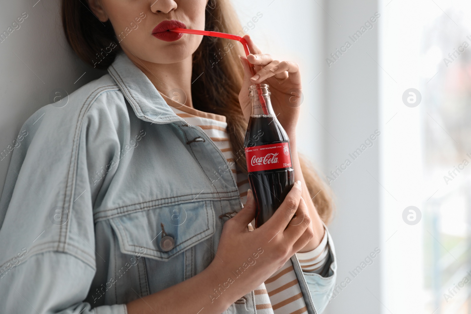 Photo of MYKOLAIV, UKRAINE - NOVEMBER 28, 2018: Young woman with bottle of Coca-Cola indoors, closeup. Space for text