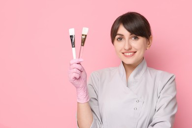 Cosmetologist with cosmetic brushes on pink background