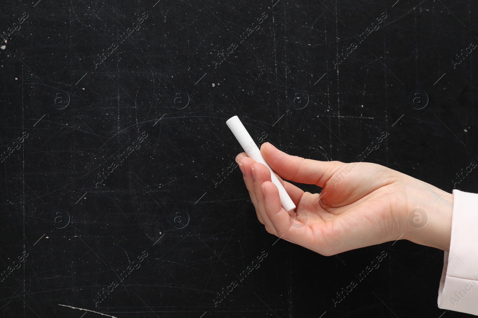 Photo of Teacher writing with chalk on black chalkboard, closeup. Space for text