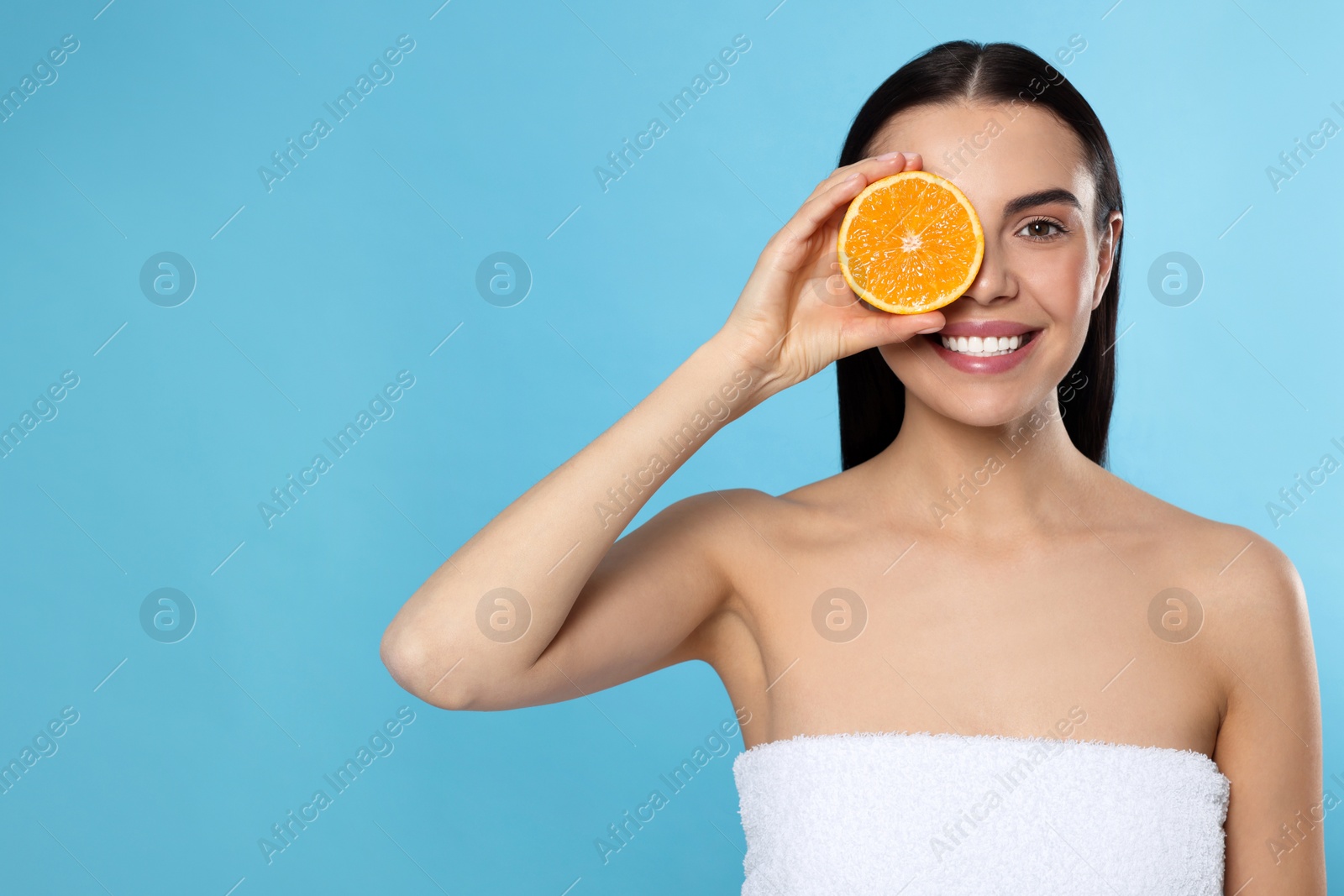 Photo of Woman holding half of orange on light blue background, space for text. Spa treatment