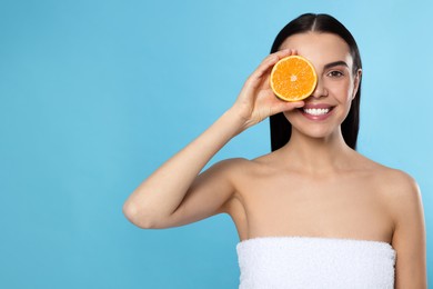 Woman holding half of orange on light blue background, space for text. Spa treatment