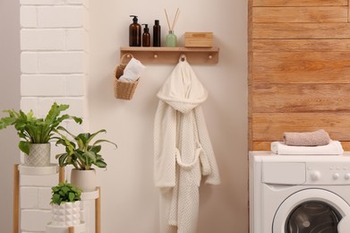 Photo of Wooden shelf with toiletries and robe on beige wall in bathroom. Interior design