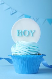 Photo of Beautifully decorated baby shower cupcake with cream and boy topper on light blue background