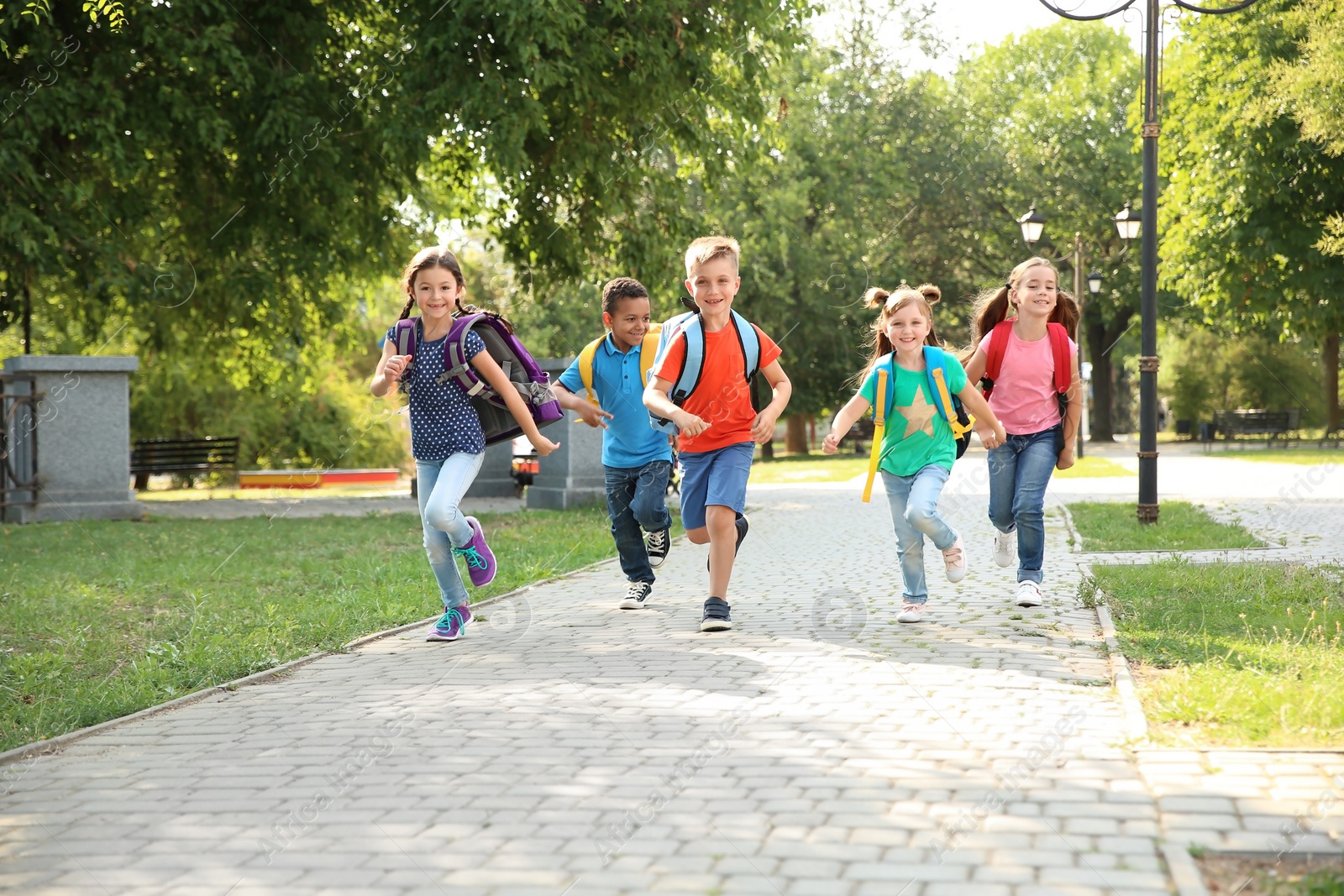 Photo of Cute little children with backpacks running outdoors. Elementary school