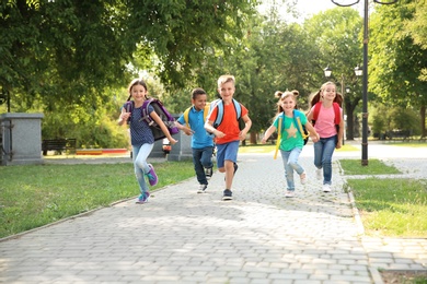 Photo of Cute little children with backpacks running outdoors. Elementary school