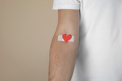 Blood donation concept. Man with adhesive plaster on arm against beige background, closeup. Space for text