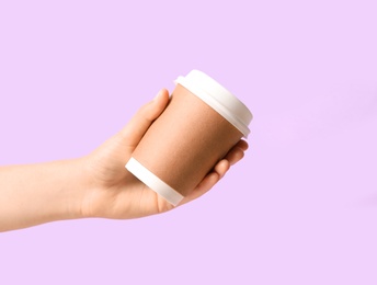 Woman holding takeaway paper coffee cup on violet background, closeup