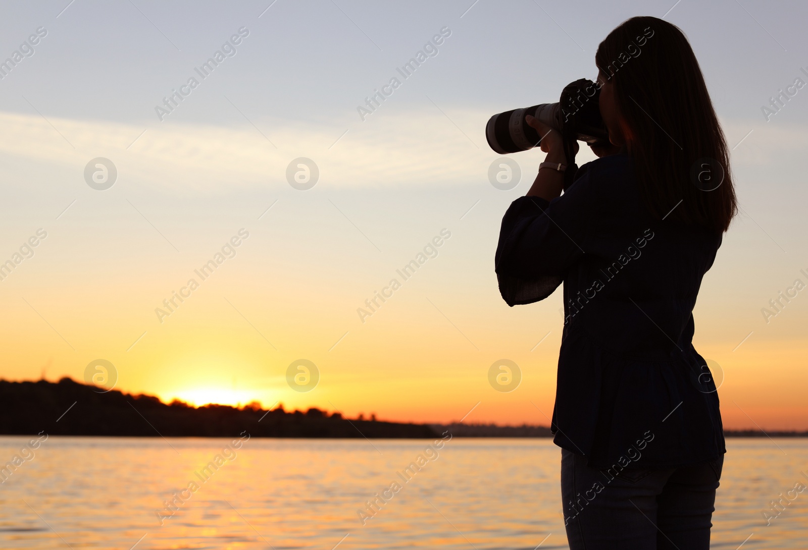 Photo of Young female photographer taking photo of riverside sunset with professional camera outdoors
