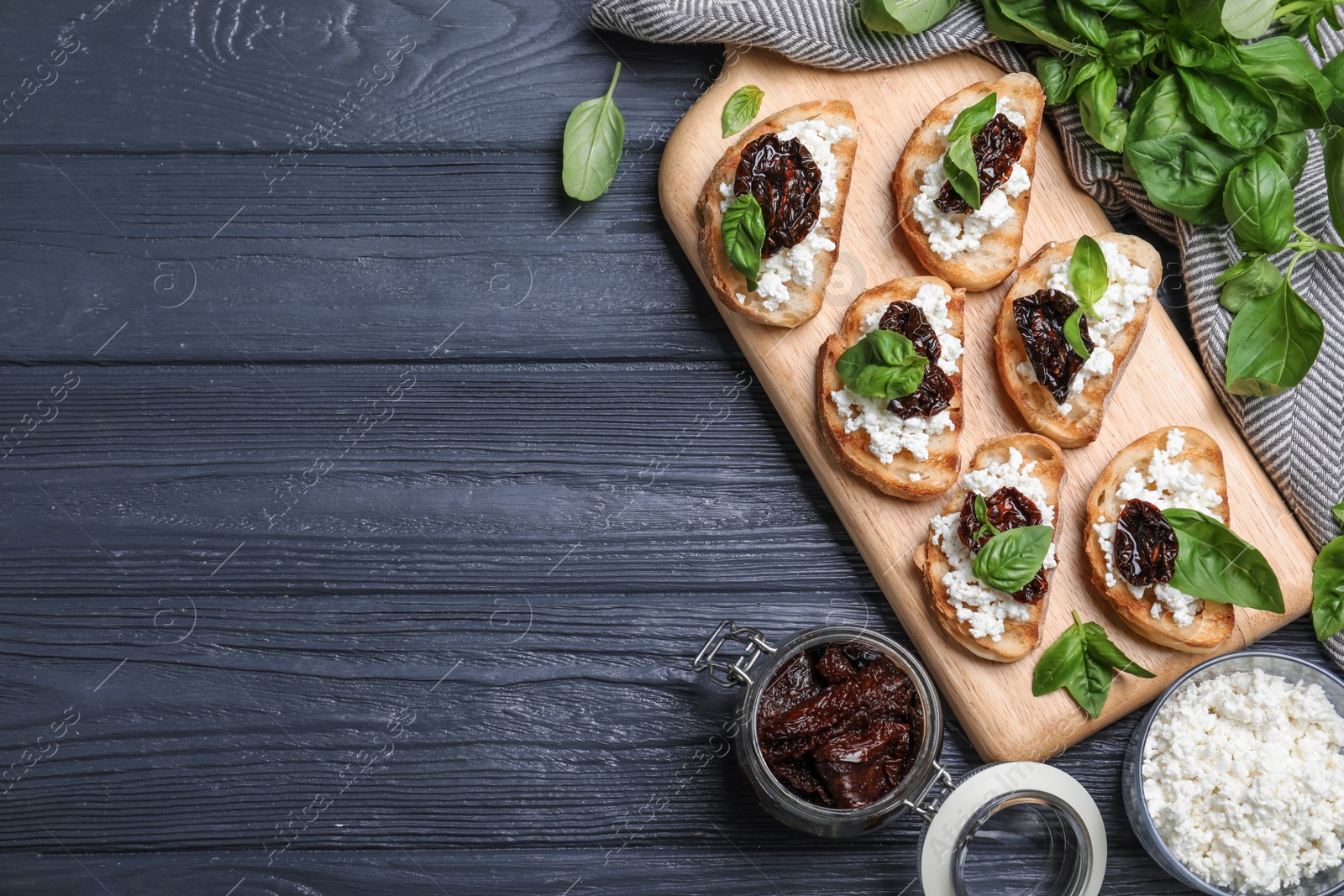 Photo of Flat lay composition of tasty bruschettas with dried tomatoes and cheese on dark grey wooden table. Space for text