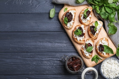 Photo of Flat lay composition of tasty bruschettas with dried tomatoes and cheese on dark grey wooden table. Space for text