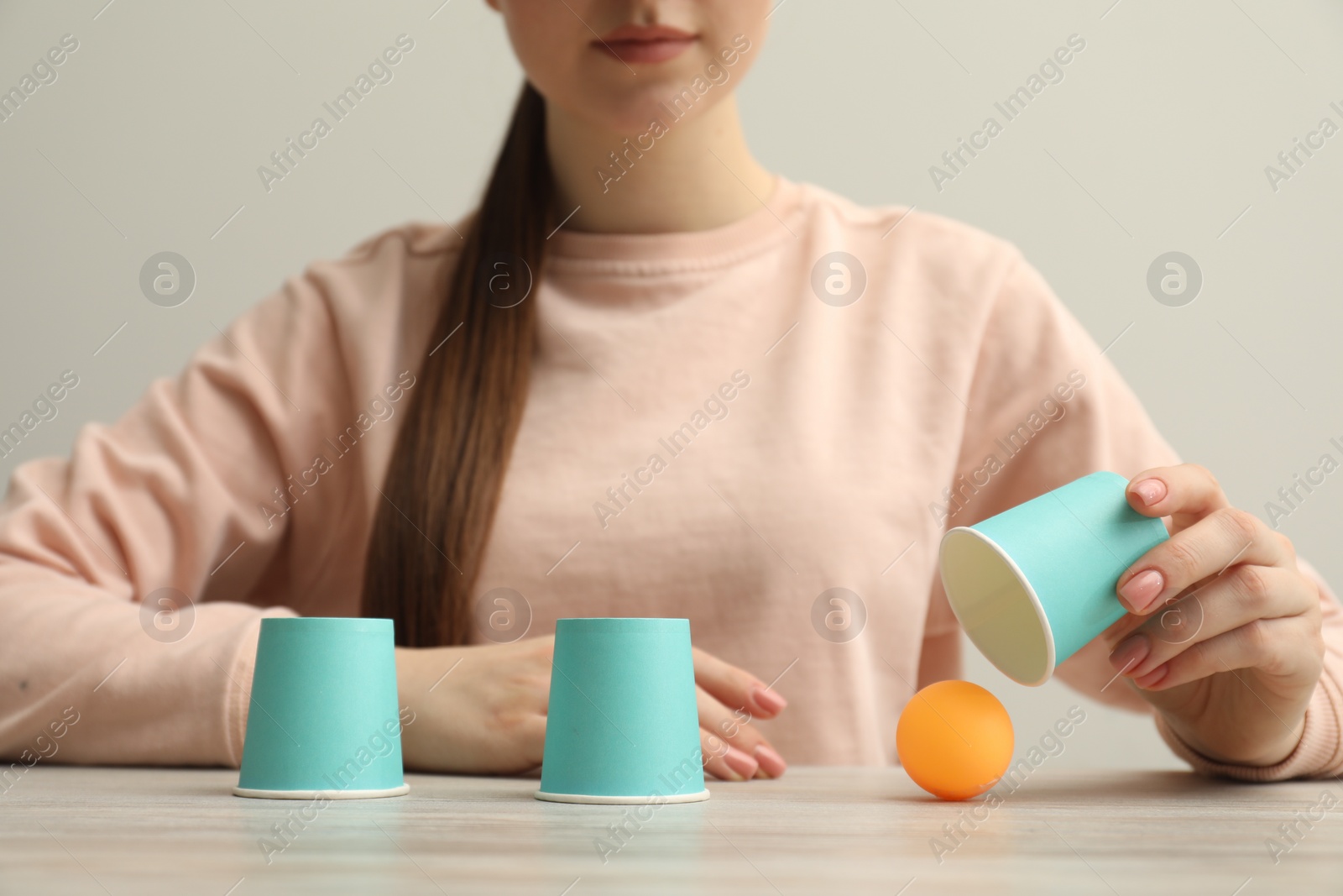 Photo of Shell game. Woman showing ball under cup at wooden table, closeup