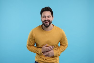 Handsome young man laughing on light blue background