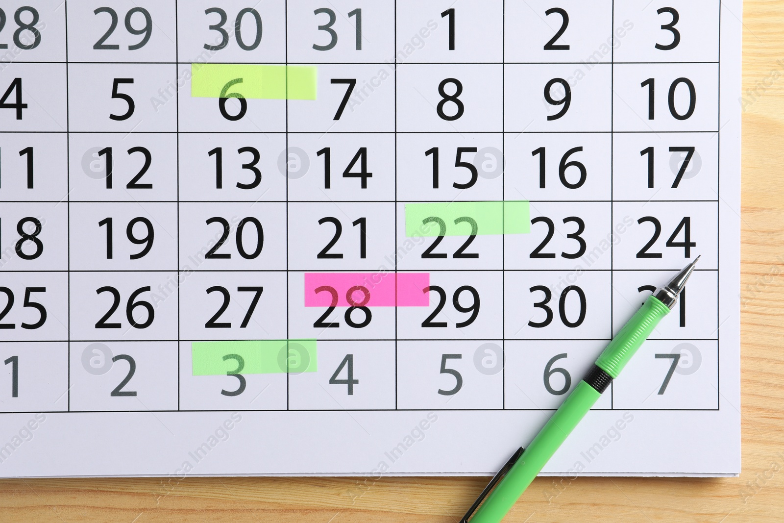 Photo of Timetable. Calendar page with marked dates and pen on wooden table, top view