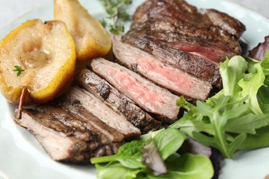 Photo of Pieces of delicious roasted beef meat, caramelized pear and greens on plate, closeup