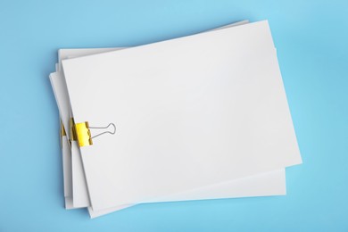 Photo of Many sheets of paper with golden clips on light blue background, top view