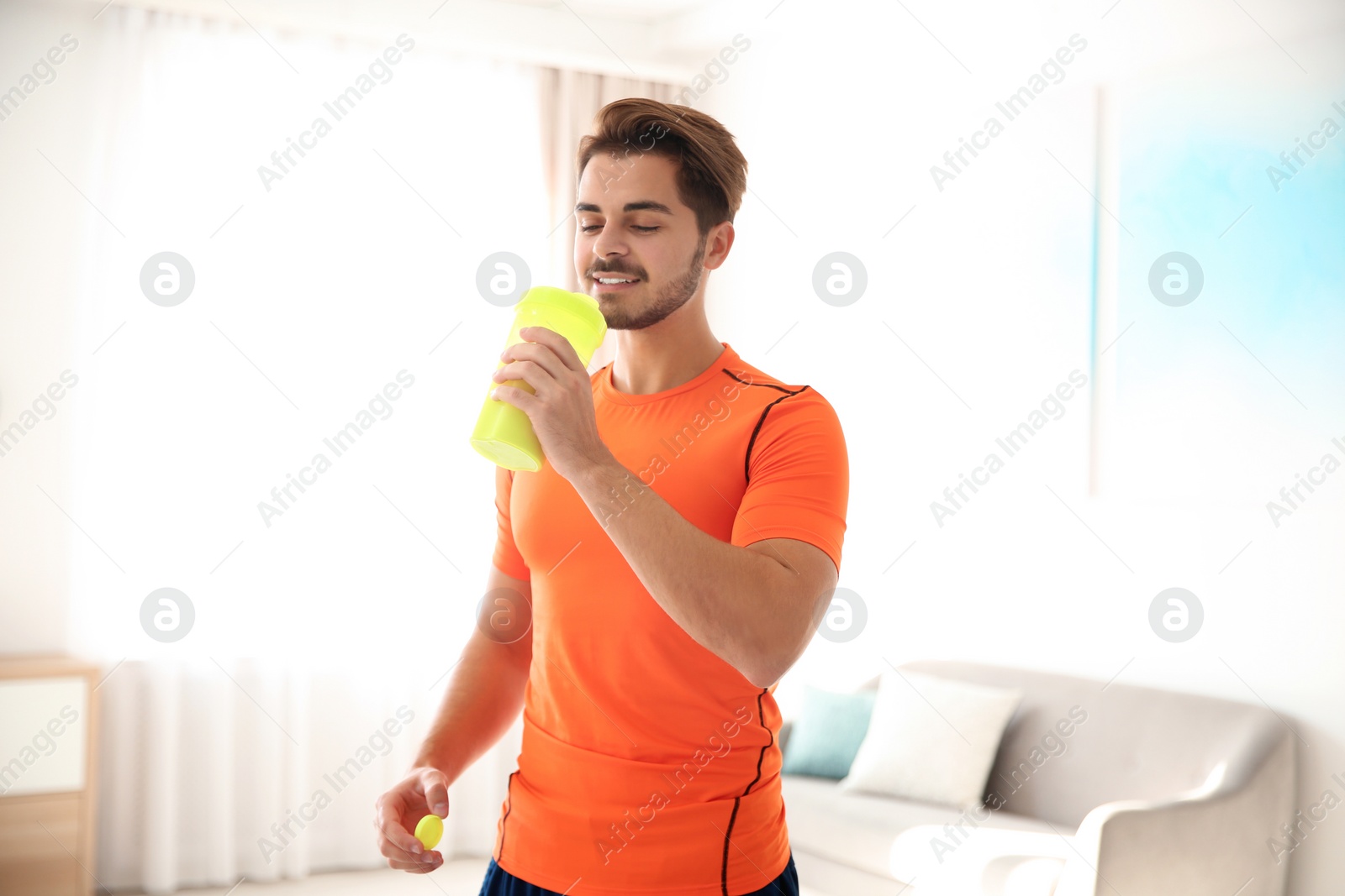 Photo of Young sporty man with bottle of protein shake at home