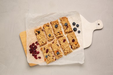 Photo of Tasty granola bars, dried cherries and blueberries on light gray textured table, top view