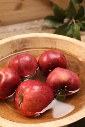 Photo of Fresh red apples in bowl with water on table