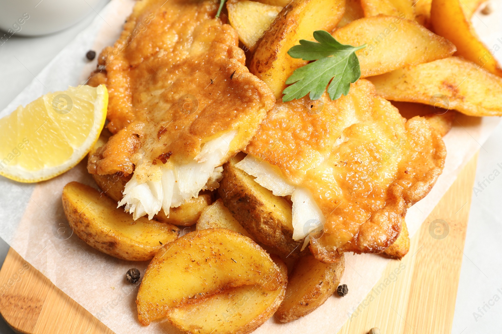 Photo of British traditional fish and potato chips on wooden board, closeup